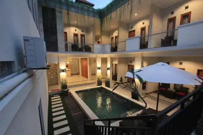 a building with a swimming pool and an umbrella at Tom Guest House in Legian