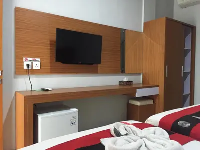 a room with two beds and a television on a wall at Tom Guest House in Legian