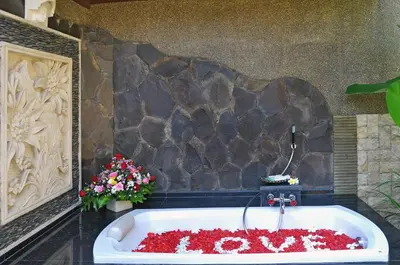 a bath tub filled with red flowers next to a stone wall at Bali Aroma Exclusive Villas in Seminyak