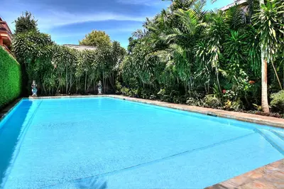 a large blue swimming pool in a yard with trees at Raja Gardens Hotel in Seminyak
