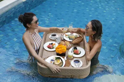 two women sitting at a table in a swimming pool at Alaya Dedaun Kuta in Legian