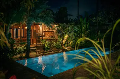 a swimming pool in a garden at night at Kubu Kayu Villas in Seminyak