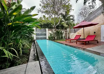 a swimming pool with two red chairs and an umbrella at Bali Island Villas and Spa Seminyak in Seminyak