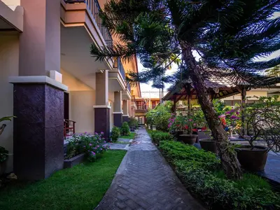 a walkway in a courtyard with a palm tree and flowers at Yulia Beach Inn Kuta in Kuta