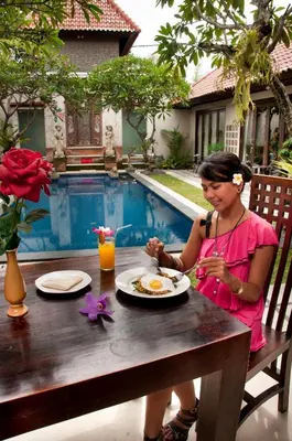 a woman sitting at a table with a plate of food at Sindhu Mertha Suite in Sanur