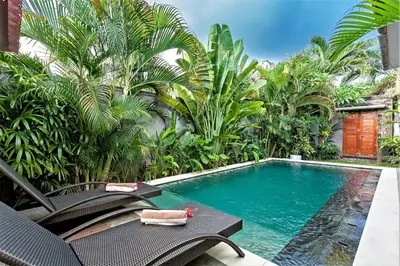 a swimming pool in a garden with chairs and trees at Rumah Indah Villa in Seminyak