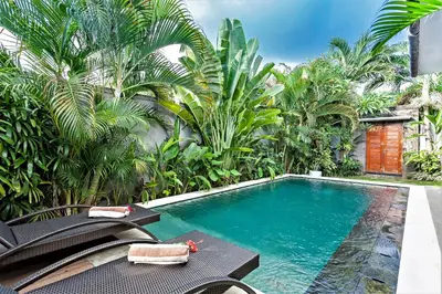 a swimming pool in a garden with palm trees at Rumah Indah Villa in Seminyak