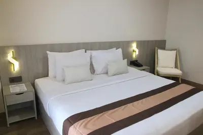 a bedroom with a large white bed with two chairs at Grand Santhi Hotel in Denpasar