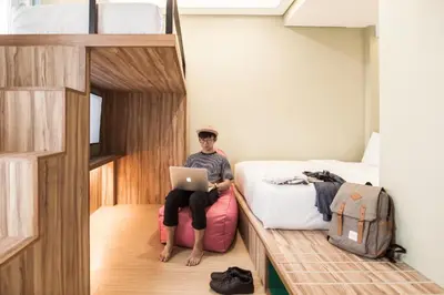 a man sitting on a suitcase in a bedroom with a laptop at Cara Cara Inn in Kuta