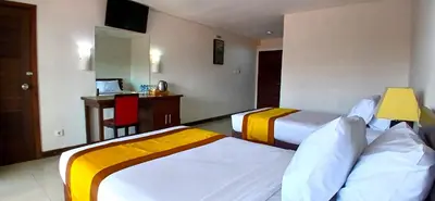 a hotel room with two beds and a desk at Nirmala Hotel & Convention Centre in Denpasar