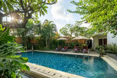 a swimming pool in a yard with chairs and trees at Pondok Sari Kuta in Kuta