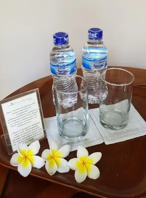 two bottles of water and two glasses and flowers on a table at Hotel Puri Bambu in Jimbaran