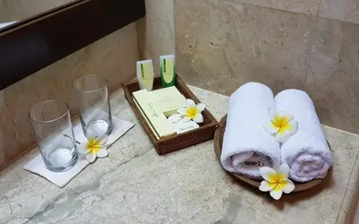a bathroom with towels and glasses and flowers on a counter at Hotel Puri Bambu in Jimbaran