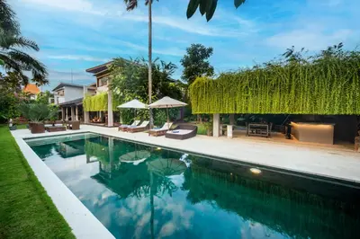 a swimming pool with chairs and umbrellas next to a house at Kamehameha Luxury Villa in Seminyak