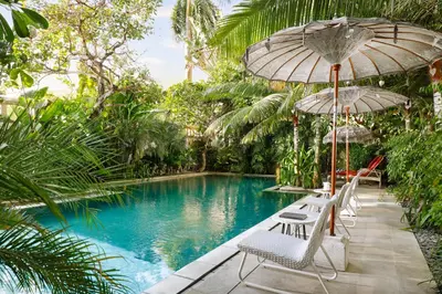 a pool with chairs and umbrellas next to a resort at Sara Residence by Nakula in Legian