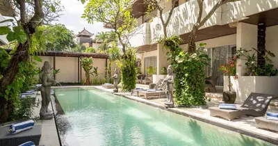 a swimming pool in front of a house with trees at Swiss-Belcourt Sunset in Seminyak