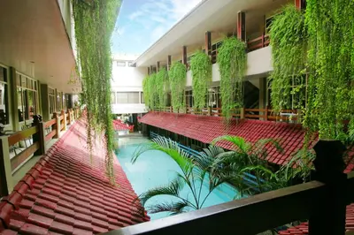 a building with a swimming pool with red seats and plants at Hotel Karthi Kuta in Kuta