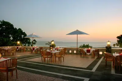 a restaurant with tables and chairs with the ocean in the background at Pelangi Bali Hotel & Spa in Seminyak