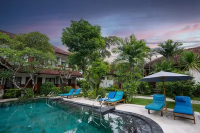 a swimming pool with blue chairs and an umbrella at Hotel Sinar Bali Legian in Legian