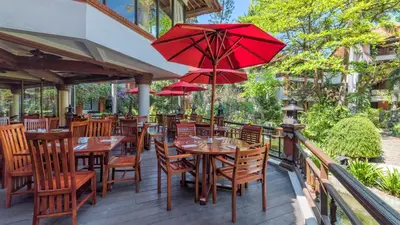 an outdoor restaurant with tables and chairs with red umbrellas at Bali Garden Beach Resort in Kuta