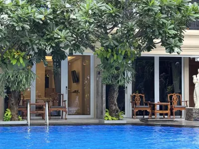 a pool with chairs and trees in front of a building at Green Garden Hotel in Kuta