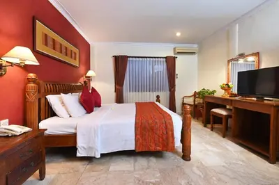 a bedroom with a bed and a desk and a television at Puri Dewa Bharata Hotel & Villas in Legian