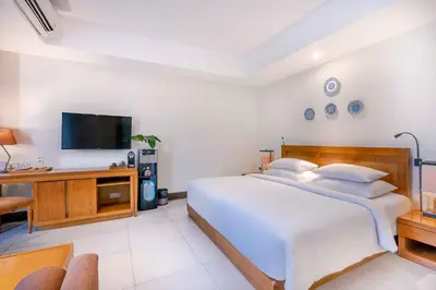 a white bedroom with a large bed and a tv at Rama Garden Hotel Bali in Legian