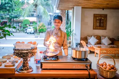 a man cooking food on a stove in a living room at Rama Garden Hotel Bali in Legian