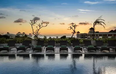 a group of chairs sitting by a pool at sunset at Champlung Mas Hotel Legian in Legian