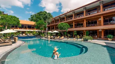 a woman is standing in a swimming pool in front of a hotel at Wina Holiday Villa Kuta Bali in Kuta