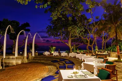 a restaurant with white tables and chairs at night at The Oberoi Beach Resort, Bali in Seminyak