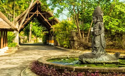 a statue sitting in a pond in a garden at The Oberoi Beach Resort, Bali in Seminyak