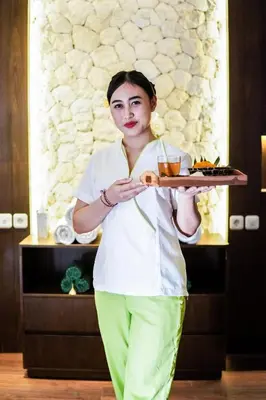 a woman holding a tray with food on it at FuramaXclusive Ocean Beach Seminyak Bali in Legian