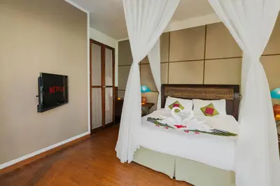 a bedroom with a bed with white curtains and a tv at Desamuda Village by Pertama Management in Seminyak