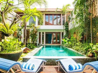 a swimming pool in a garden with two chairs and a house at Umah Watu Villas in Seminyak