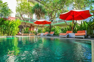 a swimming pool with umbrellas and chairs and a building at Capital O 1666 Grand Pudjawan Hotel Near Kuta Beach in Kuta