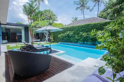 a pool with chairs and an umbrella next to a house at Kembali Villas in Seminyak