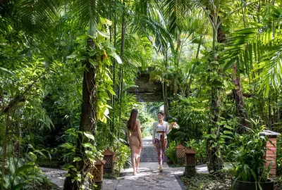 two women walking through a garden with palm trees at Tonys Villas & Resort Seminyak - Bali in Seminyak