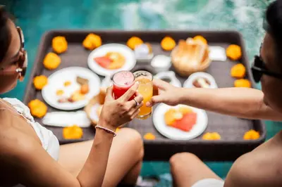 two women holding drinks in front of a tray of food at Tonys Villas & Resort Seminyak - Bali in Seminyak