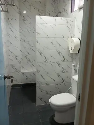 a white bathroom with a toilet and marble walls at City Garden Bali Dwipa Hotel, Kuta in Kuta