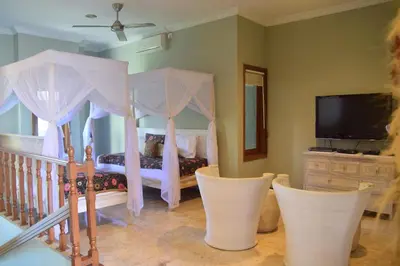 a bedroom with a canopy bed with chairs and a tv at Villa Putu Mira By Maha Bali in Kuta