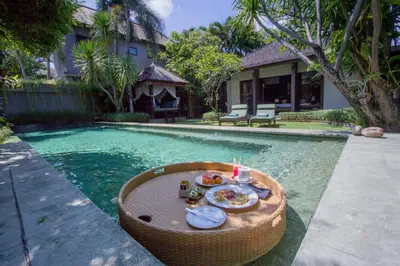 a table with a plate of food next to a swimming pool at Chimera Villas in Seminyak