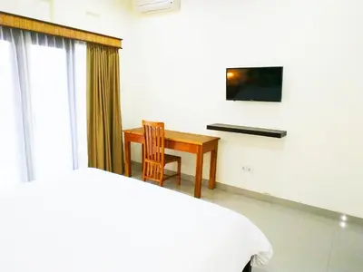 a bedroom with a bed and a desk and a television at Dwiputra Guest House in Canggu