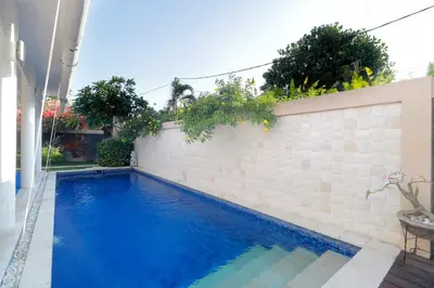 a blue swimming pool next to a white brick wall at Heliconia Villa in Seminyak