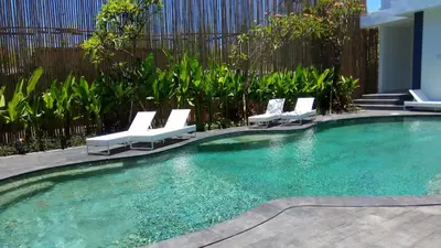 a swimming pool with white lounge chairs in a yard at The Bali Bubble in Sanur