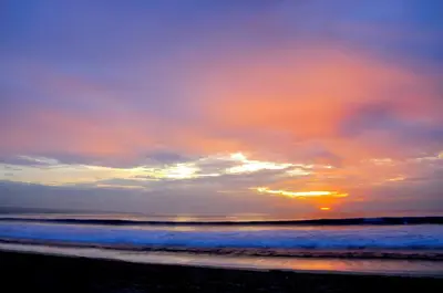 a sunset on a beach with the ocean at Guest House Matahari in Kuta