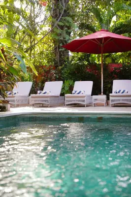 a pool with chairs and an umbrella and water at Villa Hangat in Seminyak