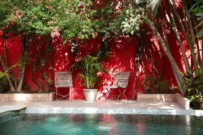 a swimming pool with two chairs and a red wall at Villa Hangat in Seminyak