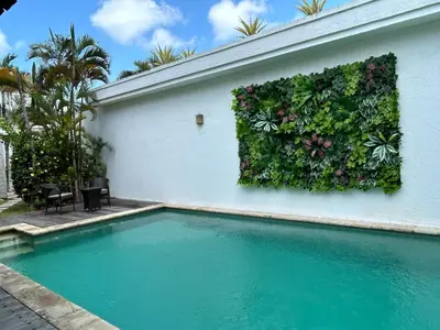 a swimming pool next to a white wall with a plant at Artemis Villa Hotel in Seminyak