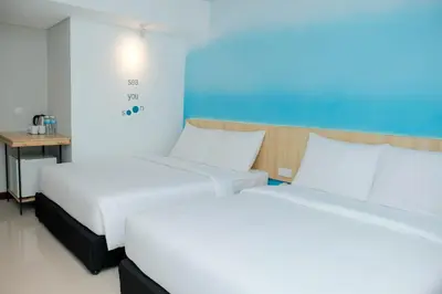 two white beds in a room with a table at Bloo Bali Hotel in Legian
